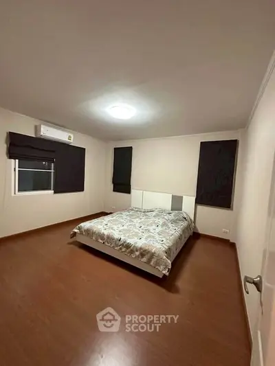 Spacious bedroom with modern decor and wooden flooring, featuring a comfortable bed and air conditioning.