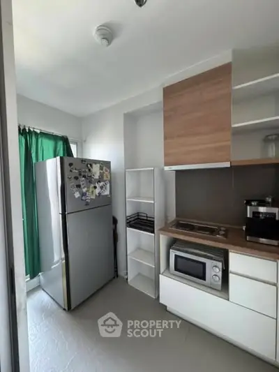 Modern kitchen with stainless steel fridge, microwave, and coffee maker in compact layout.