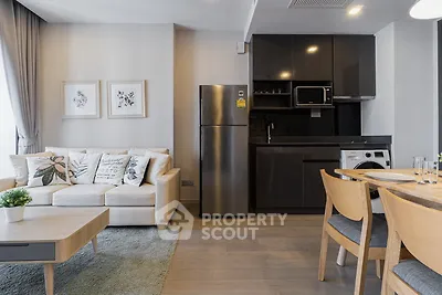 Modern living room with sleek kitchen and dining area, featuring stylish furniture and appliances.