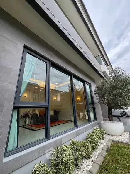 Modern building exterior with large windows and landscaped garden, showcasing elegant interior lighting.