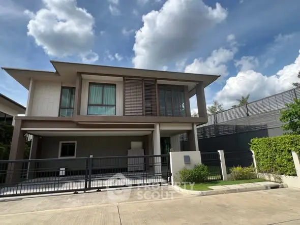 Modern two-story house with large windows and gated driveway under a clear blue sky.
