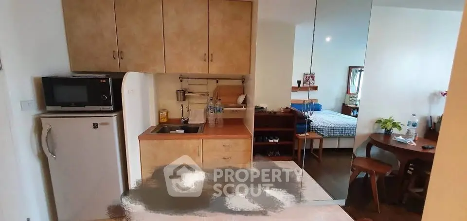 Cozy studio apartment with compact kitchen and dining area, featuring modern appliances and wooden furniture.