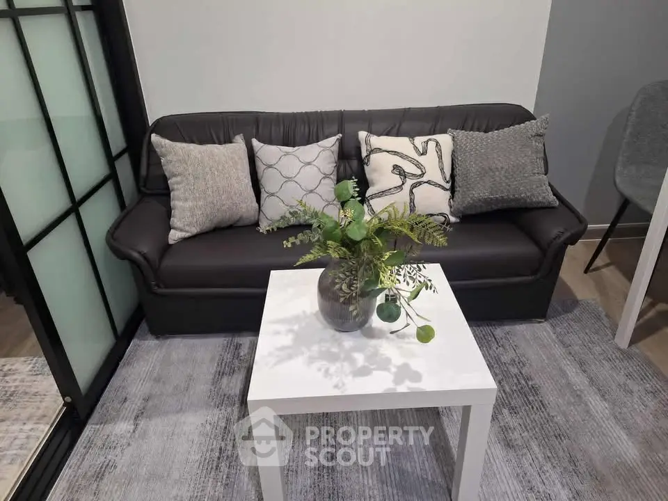 Modern living room with stylish black sofa, decorative pillows, and a chic white coffee table with a plant.