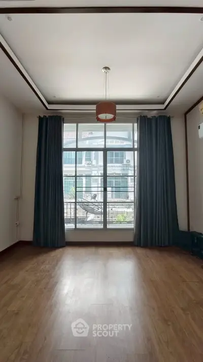 Spacious room with large window and elegant curtains, perfect for natural light.
