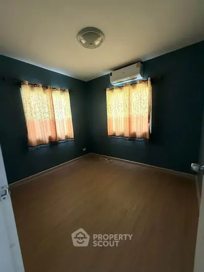Spacious bedroom with wooden flooring and natural light from two windows.