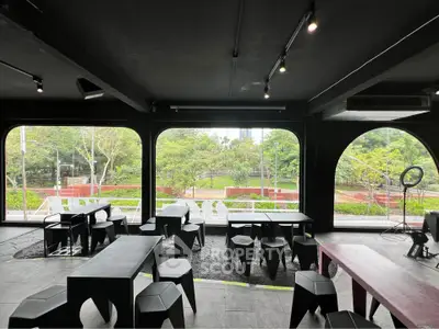 Modern interior with large windows overlooking lush garden, featuring sleek black furniture.