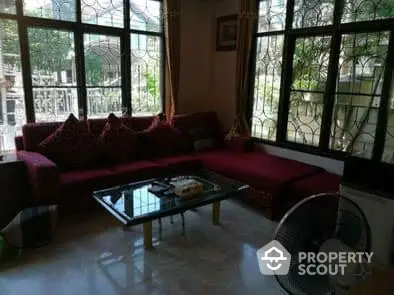 Spacious living room with large windows, plush red sofas, and a glass-top coffee table, offering a comfortable and inviting space.