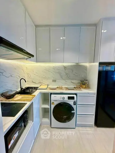 Modern kitchen with sleek appliances and marble backsplash, featuring a washing machine and ample storage.
