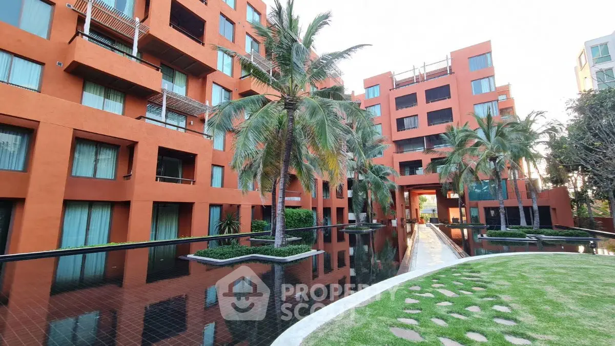 Stunning modern apartment complex with lush palm trees and reflective water feature.