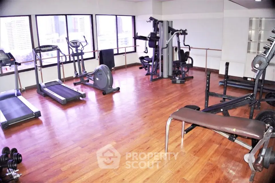 Spacious gym with modern equipment and wooden flooring in a high-rise building.