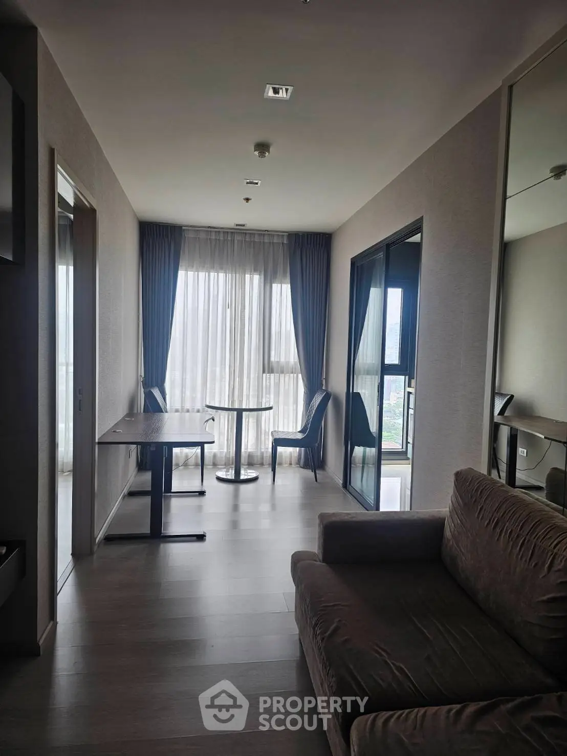 Modern apartment interior with cozy seating and dining area, featuring floor-to-ceiling windows and elegant curtains.