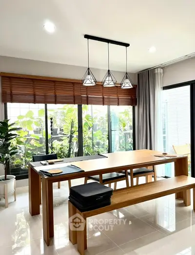 Spacious dining area with sleek wooden table, modern lighting, and a view of lush greenery through large windows, perfect for family gatherings.