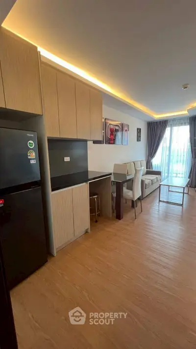 Modern living room with sleek kitchen and dining area, featuring stylish decor and natural light.