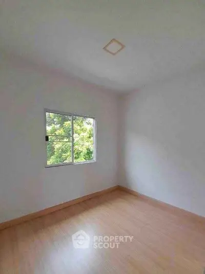 Bright empty room with wooden flooring and large window view.