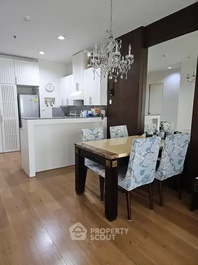 Elegant dining area with chandelier and modern kitchen in open layout apartment.