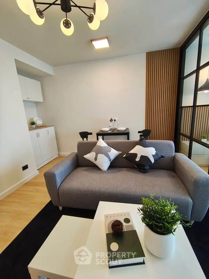Modern living room with stylish decor, featuring a cozy gray sofa, chic lighting, and a dining area in a contemporary apartment.