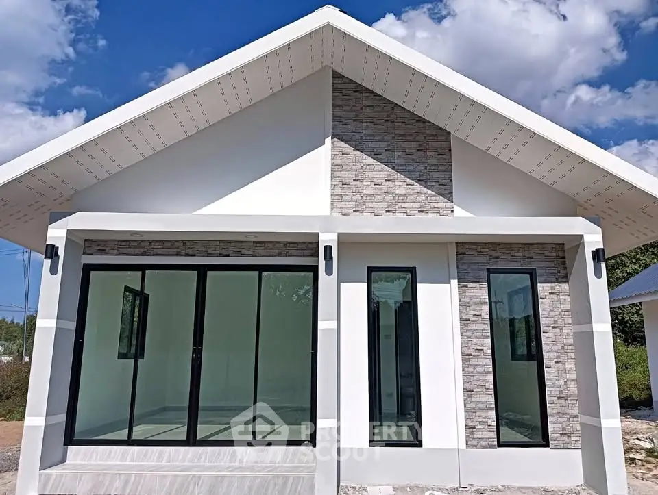 Modern single-story house with large windows and stone facade under a clear blue sky.