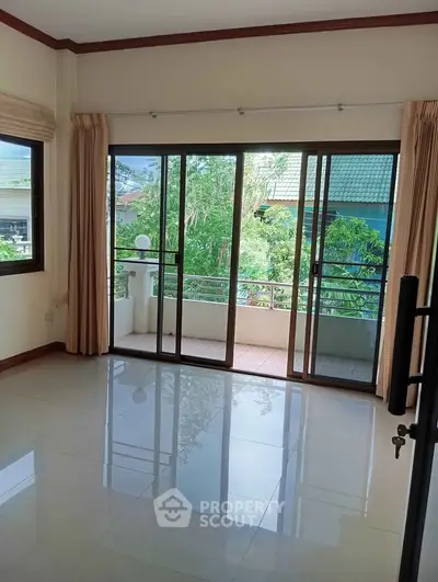 Spacious living room with large windows and balcony access, offering a serene view of lush greenery.