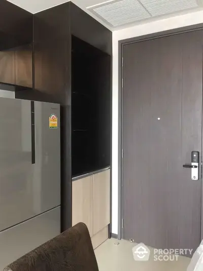 Modern apartment entrance with sleek wooden door and stainless steel fridge