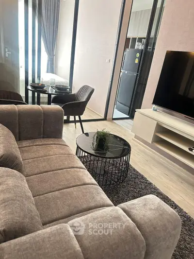 Modern living room with cozy sofa and sleek TV setup, open to dining area and kitchen.