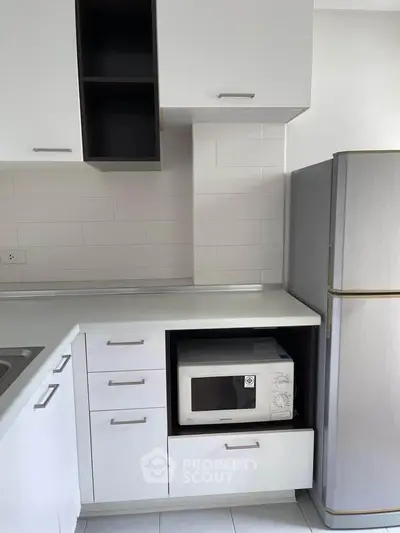 Modern kitchen with sleek white cabinets and built-in microwave, featuring a spacious fridge.
