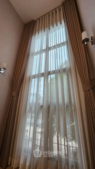 Elegant high ceiling window with luxurious curtains in a modern home interior.