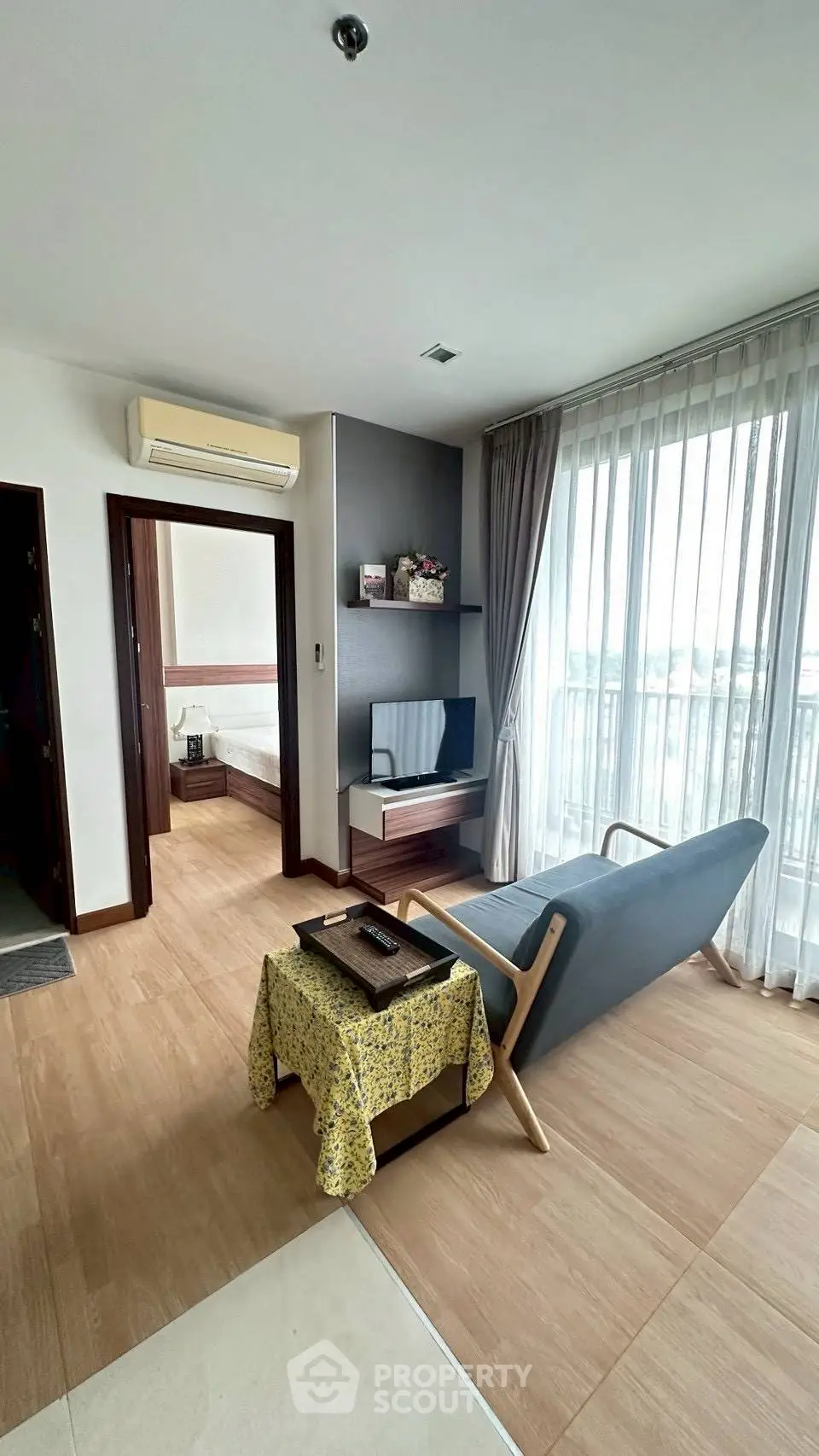 Modern living room with sleek furniture and large window offering natural light and city view.