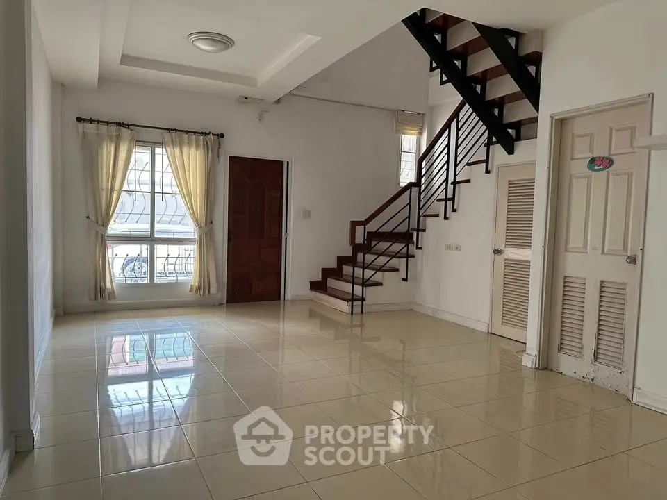 Spacious living room with staircase and large window, perfect for family gatherings.