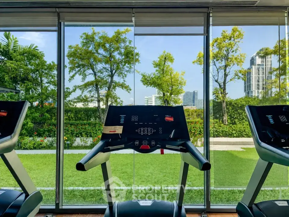 Modern gym with treadmills overlooking lush garden and cityscape view