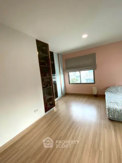 Spacious bedroom with wooden flooring and large window for natural light.