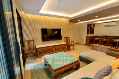 Spacious living room with modern decor and wooden furniture, featuring a large TV and cozy seating area.
