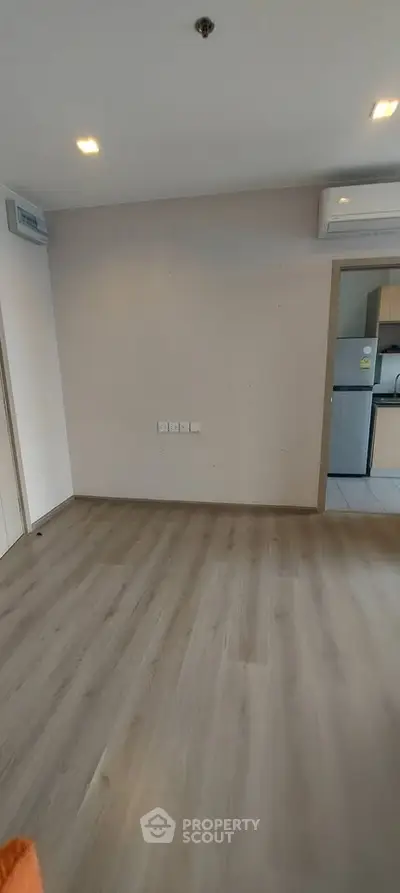 Spacious empty room with wooden flooring and modern kitchen view.