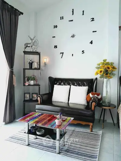 Chic living room with stylish black sofa, wall clock, and colorful coffee table, perfect for modern home decor.