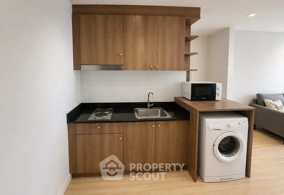 Modern compact kitchen with wooden cabinets, washing machine, and microwave in a cozy apartment.