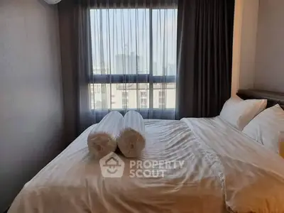 Cozy bedroom with large window and city view, featuring elegant bedding and curtains.