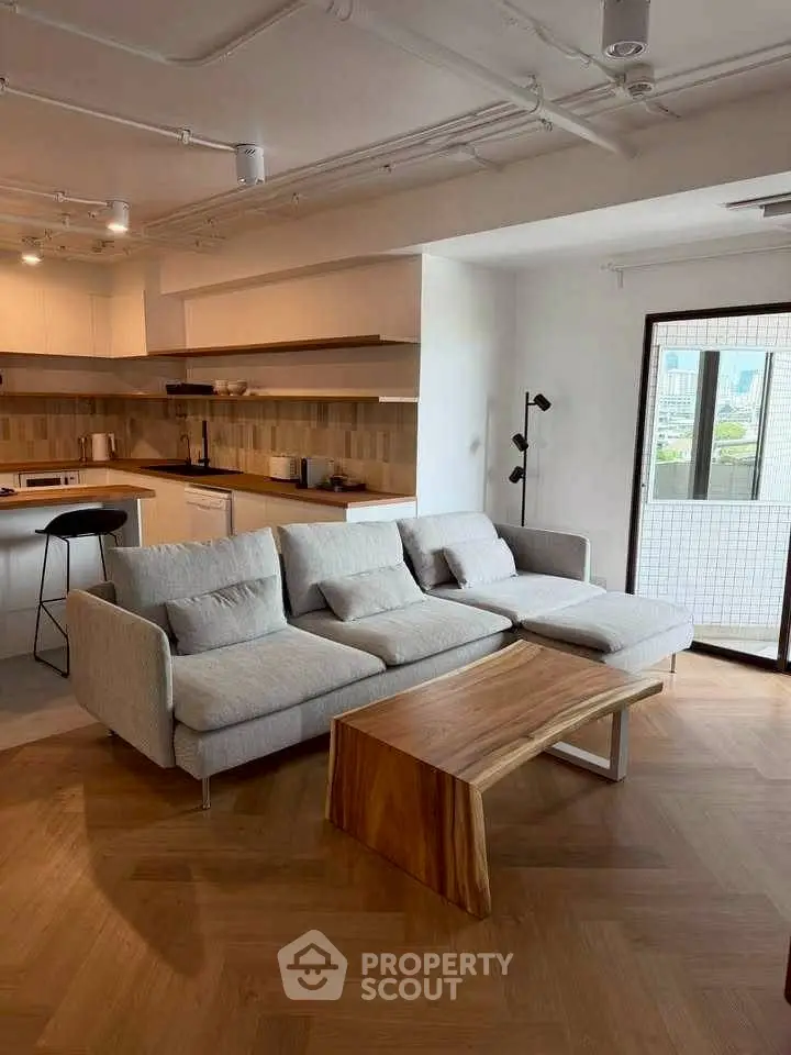 Modern living room with stylish sofa and open kitchen layout, featuring wooden flooring and natural light.