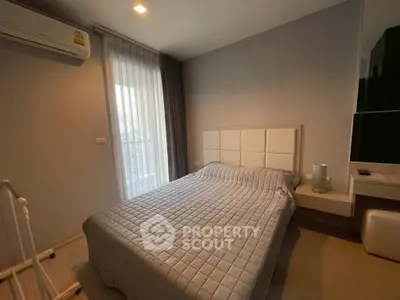 Cozy bedroom with modern decor and natural light from large window, featuring a comfortable bed and air conditioning.