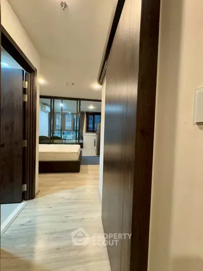 Modern apartment hallway leading to a cozy bedroom with wooden flooring and ambient lighting.