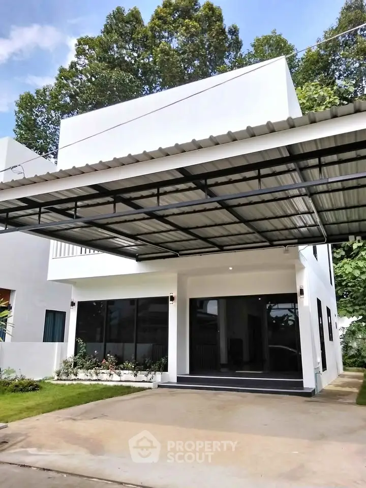 Modern two-story house with sleek design and spacious carport, surrounded by lush greenery.