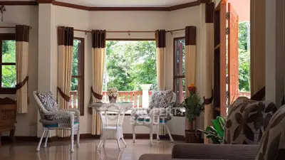 Charming living room with large windows and garden view, featuring elegant wicker furniture and cozy decor.