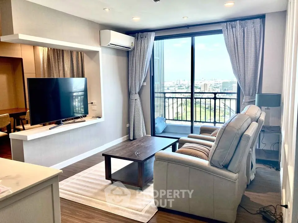 Modern living room with large window and city view, featuring cozy seating and sleek TV setup.