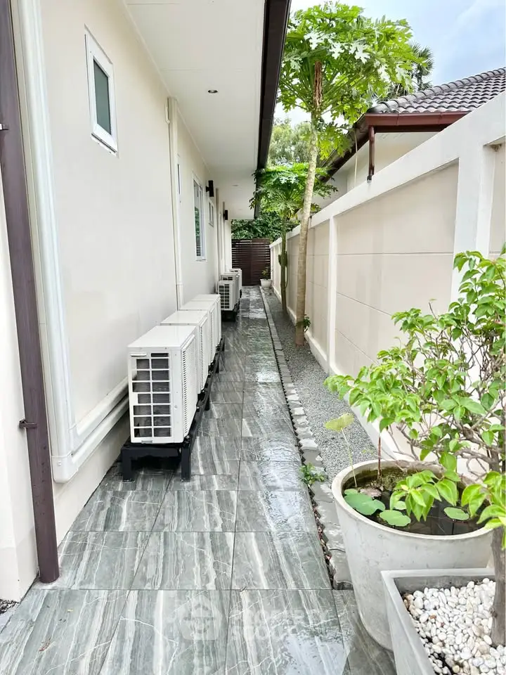 Narrow side pathway with air conditioning units and lush greenery in a modern property.