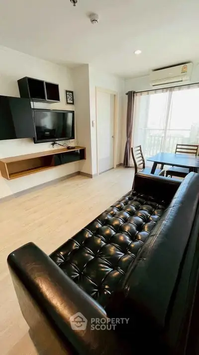 Modern living room with sleek black leather sofa and wall-mounted TV, featuring a dining area with natural light.