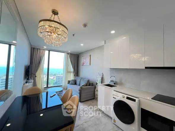 Luxurious modern living room with ocean view, elegant chandelier, and sleek kitchen appliances.