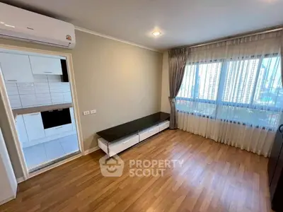 Spacious living room with large window and view of city skyline, adjacent to modern kitchen.