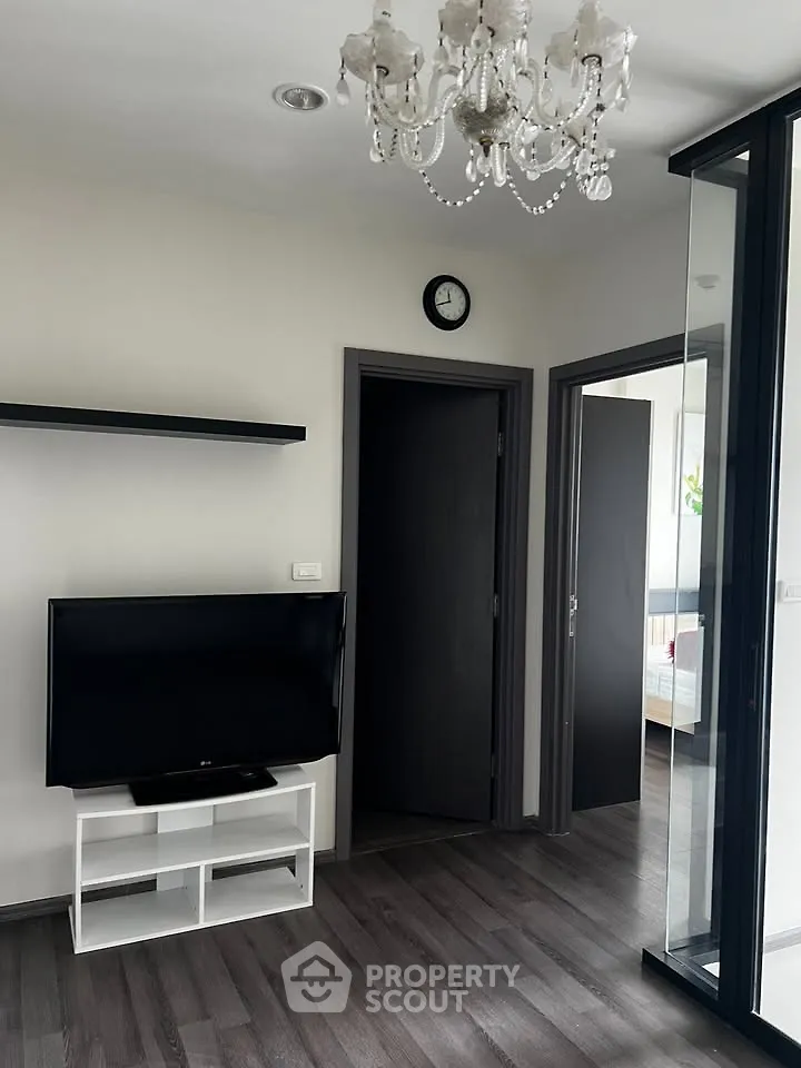 Modern living room with chandelier and TV, featuring sleek flooring and glass partition.