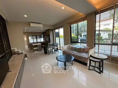 Spacious modern living room with open kitchen and large windows offering natural light and garden view.