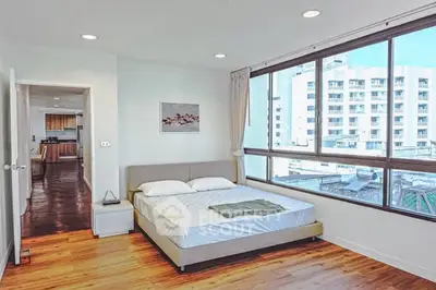 Spacious bedroom with large windows and city view, featuring modern decor and wooden flooring.