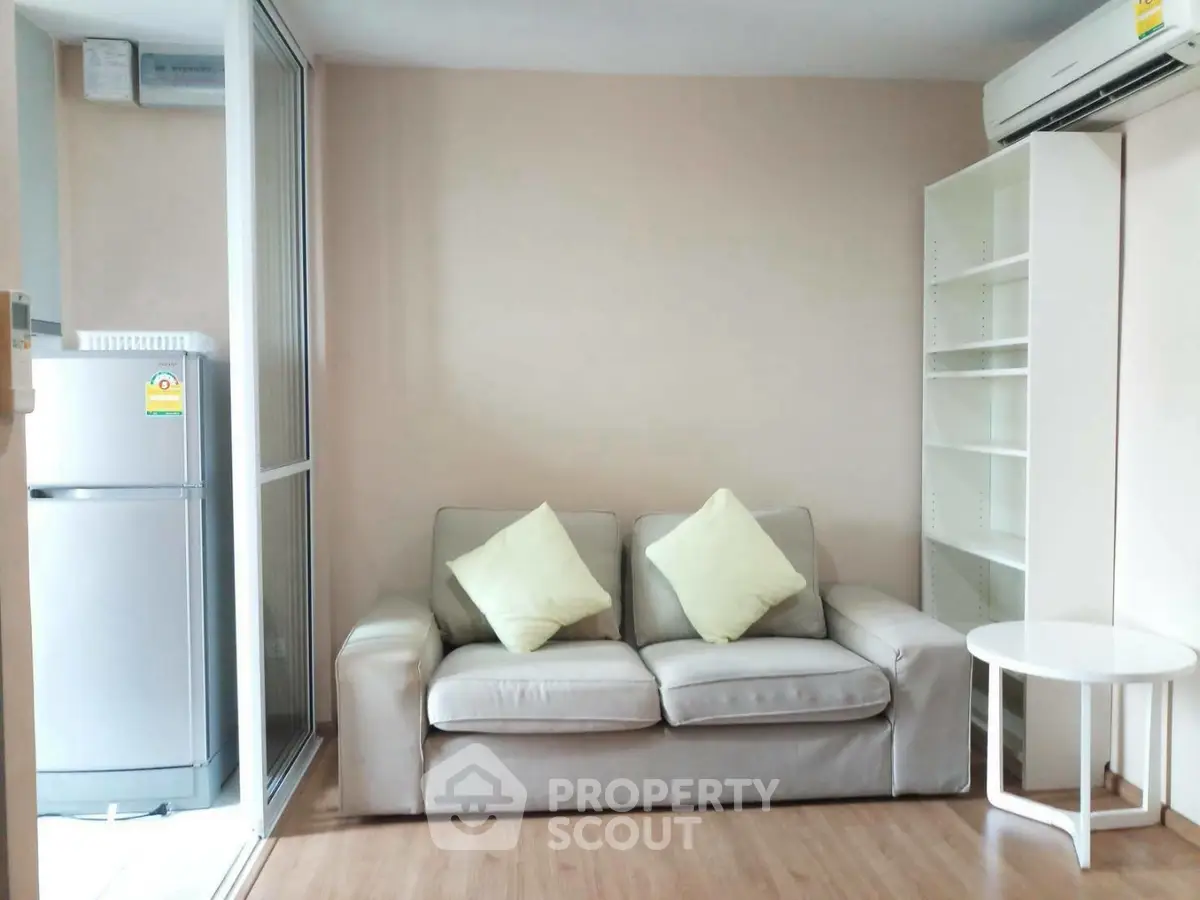 Cozy living room with modern sofa, air conditioning, and adjacent kitchen area.