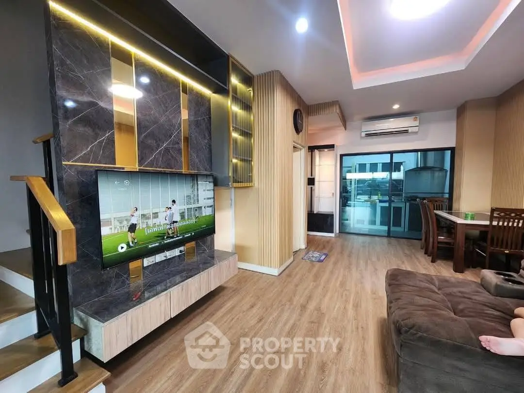 Modern living room with stylish decor, wooden flooring, and large TV, perfect for relaxation and entertainment.